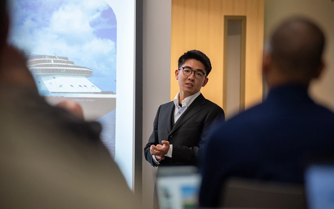A Knox student in a suit stands in front of a projector giving a presentation.