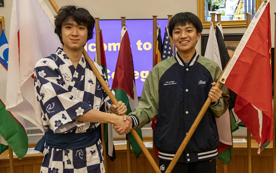 A Chinese and Japanese student shake hands and hold their home country's flags.
