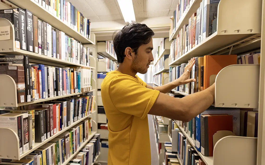 A student looks at books on shelves in the library
