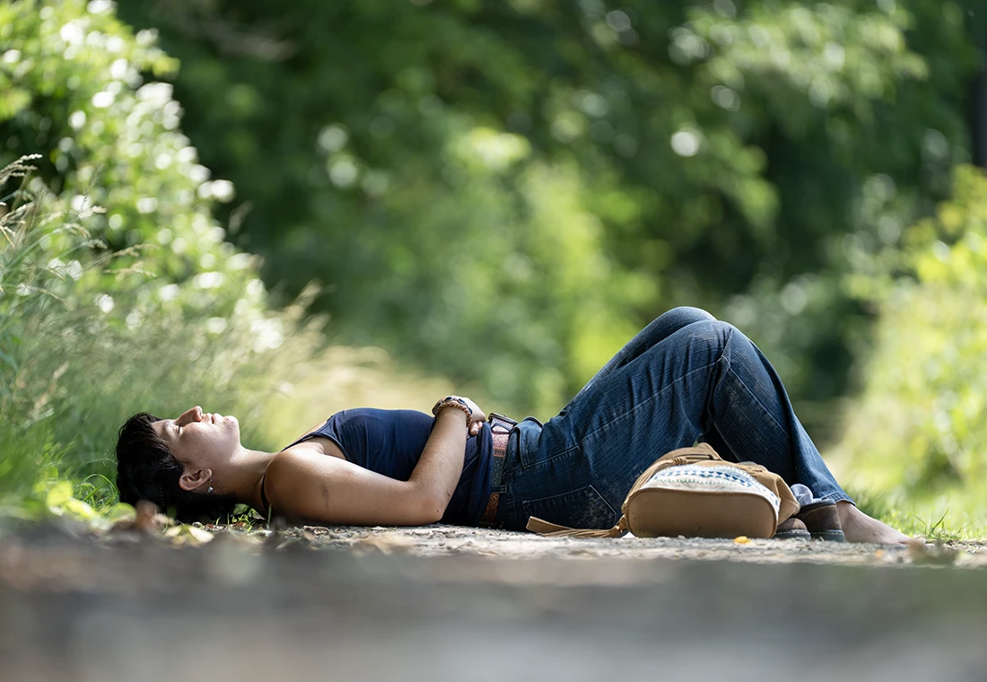A student lays on the ground in Green Oaks surrounded by different plants, and the student appears to be taking a nap.