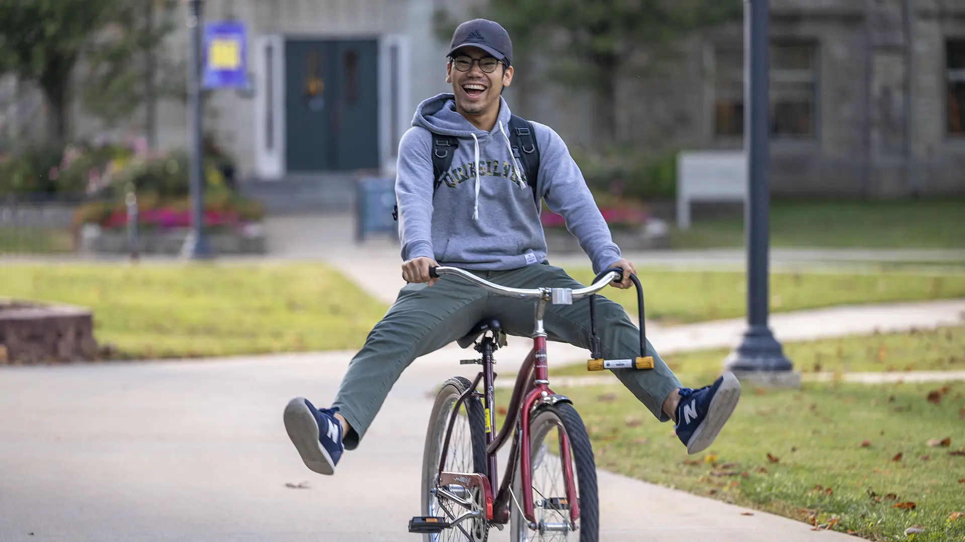 A smiling student riding a bicycle, legs outstretched, across the Knox campus.