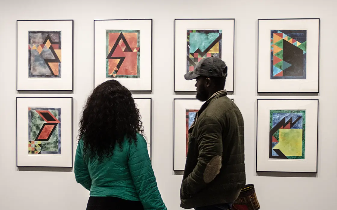Two students stand in front of a wall of art, looking at it.