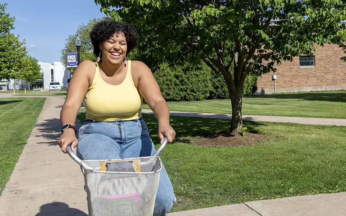 A student rides a bike across campus with a blue sky in the background.