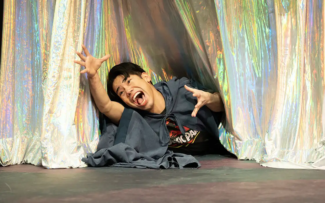 A student performing in a play is dramatically reaching for the camera.