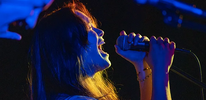 A close-up of a Knox student signing into a microphone. She is lit by purple lights.