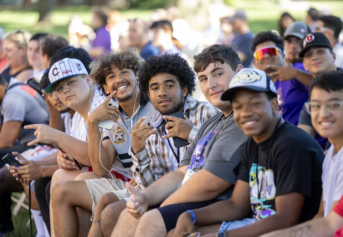 A group of students sitting in a crowd outdoors smiling at the camera.