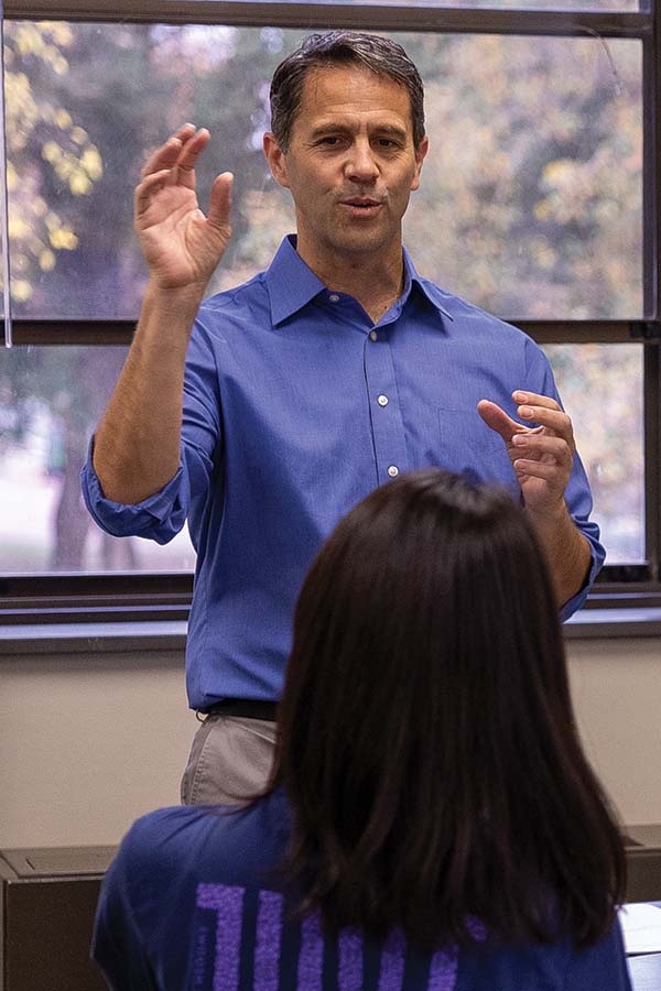 Professor Gomez teaching at the front of a classroom with a student sitting in front of him.