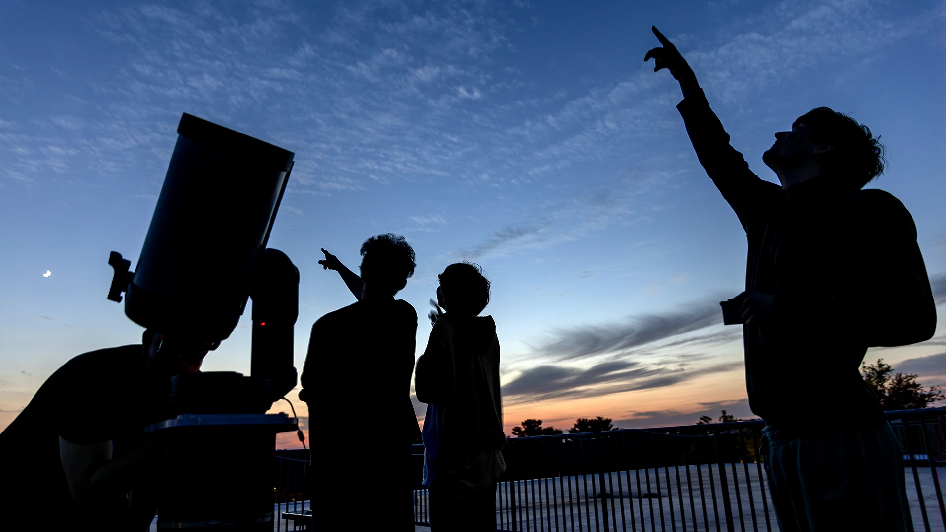 Student next to a telescope at the observatory look up at the sky.