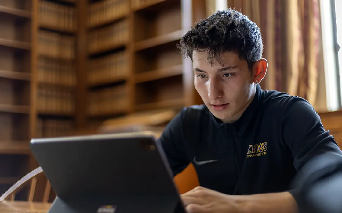 A student sitting in the library working on his laptop.