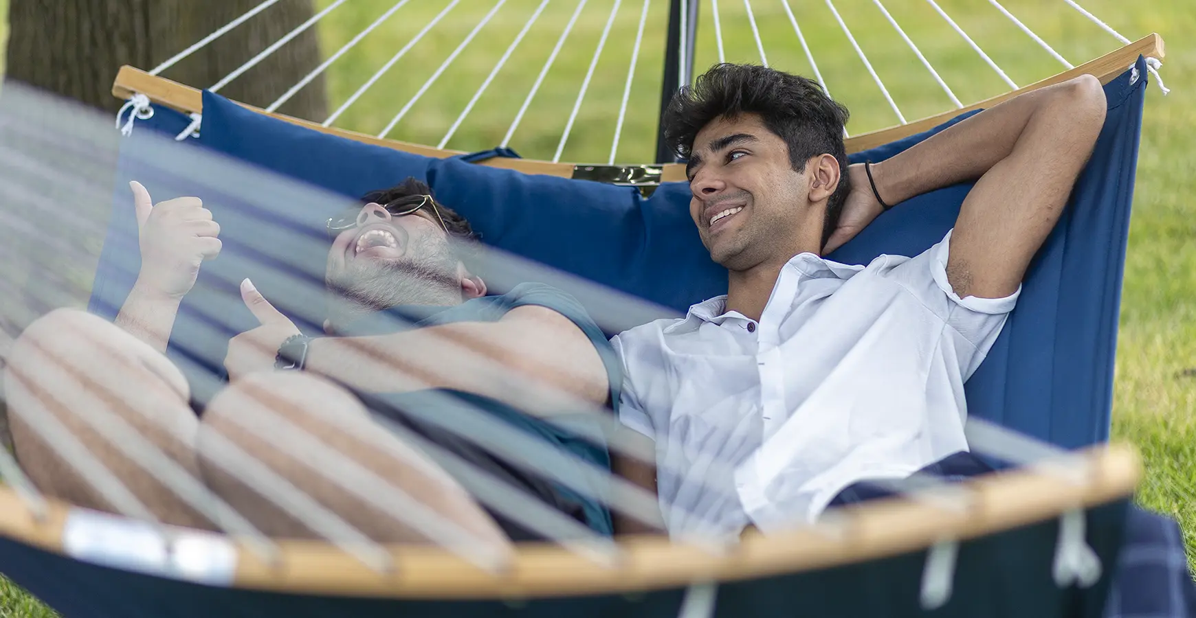 Two students laugh while laying in a hammock outside.