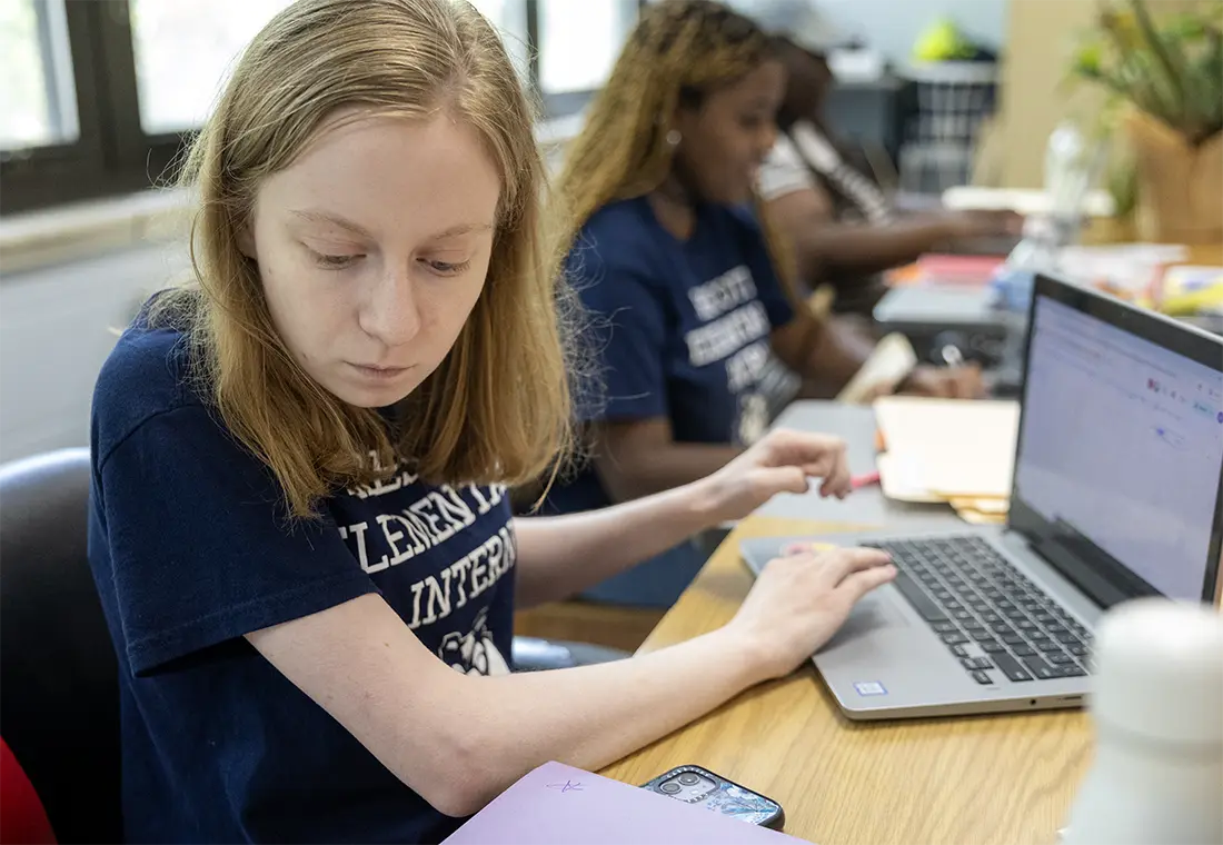 A student works on a laptop while sitting at a desk.