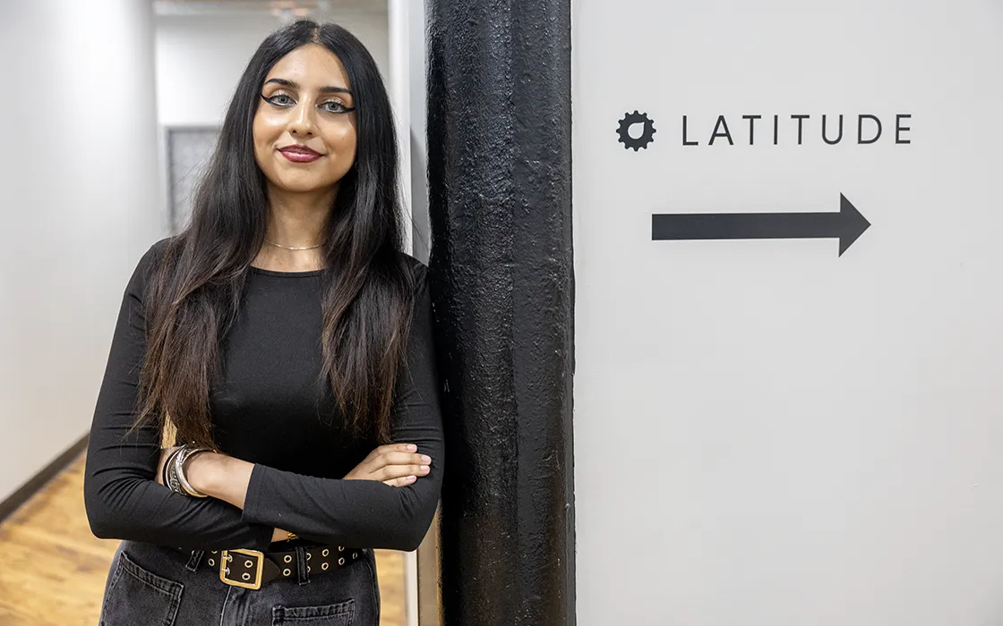 A student leans against a wall with a sign that says Latitude.