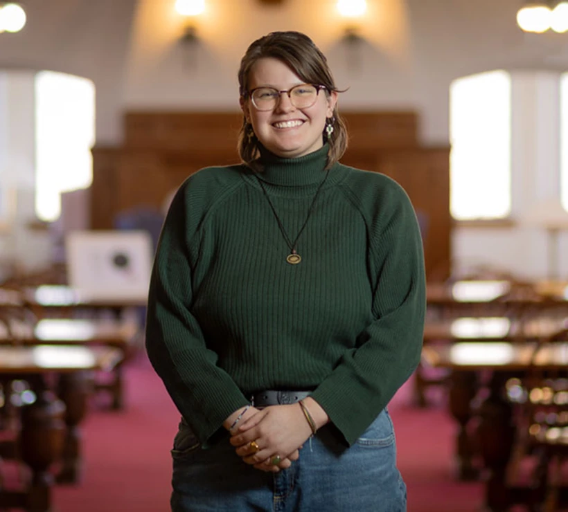 Kaitlyn smiling at the camera in the Red Room in the library.