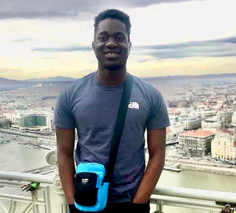 Raph standing on the balcony of a building with a town in the background.