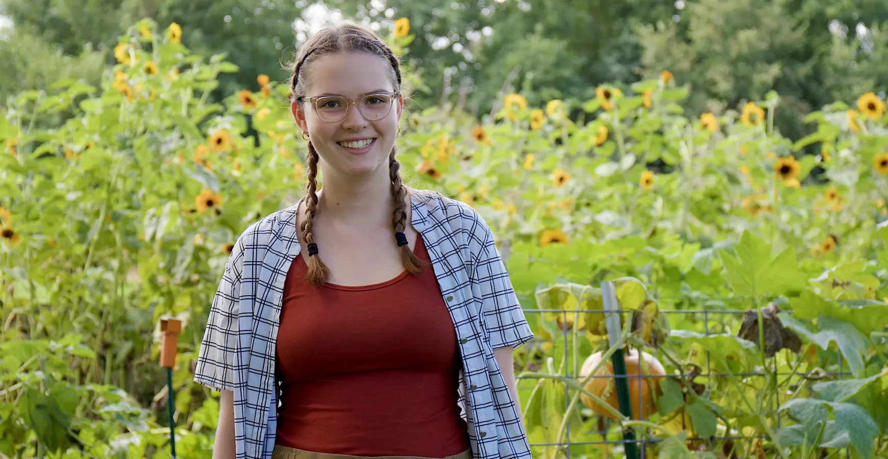 A student smiles at the camera. Behind her, sunflowers are visible.