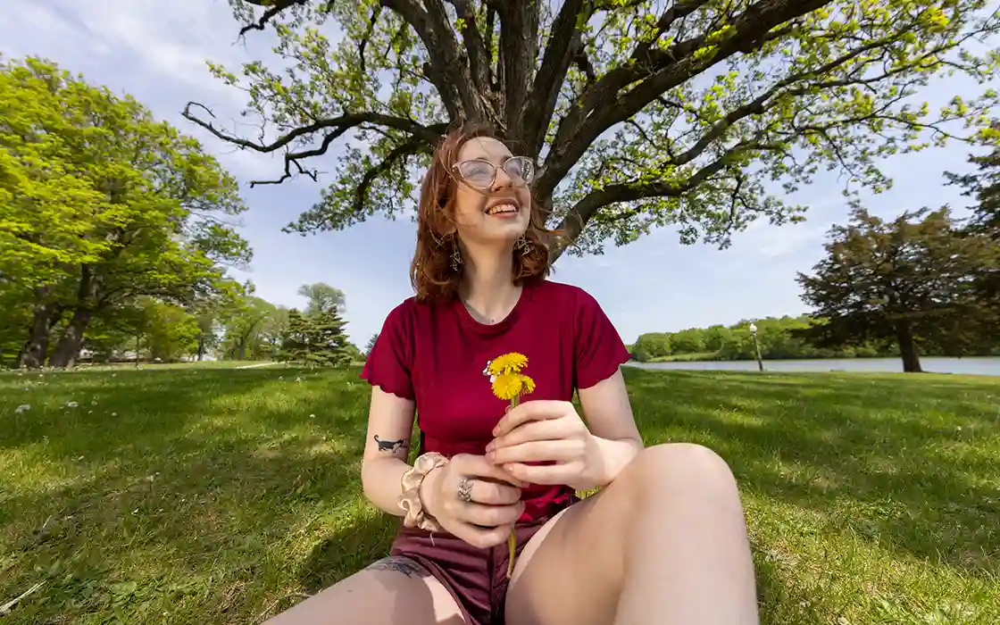 A Knox student in a red shirt sits under a tree on the South Lawn.