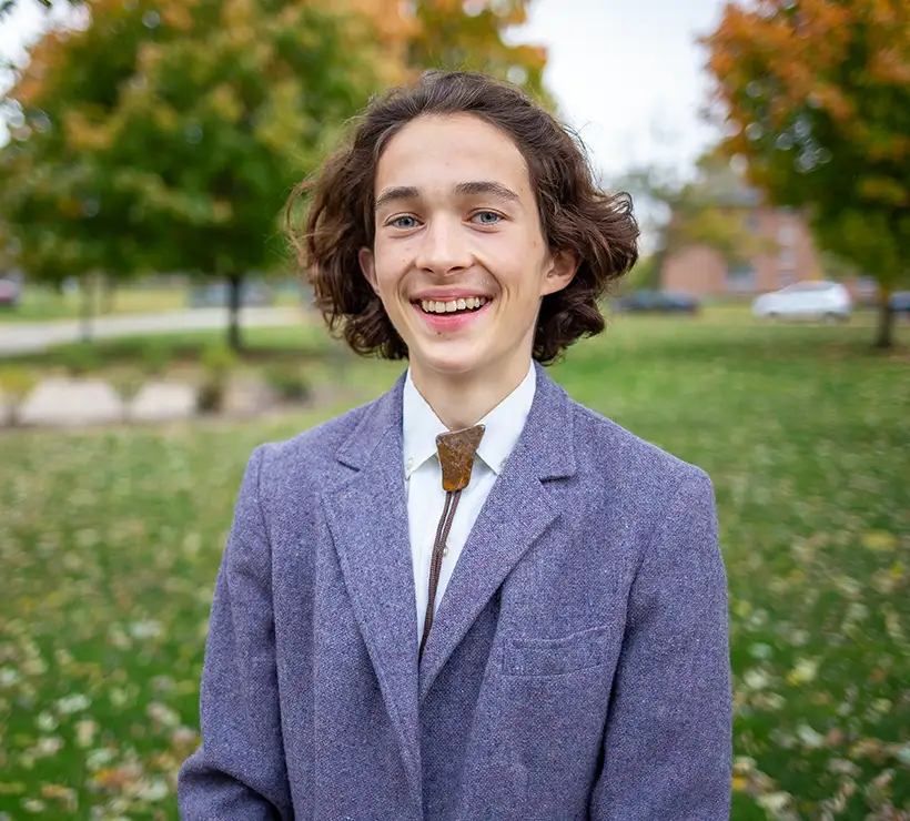 A photo of Issac Hughes wearing a suit and smiling at the camera.