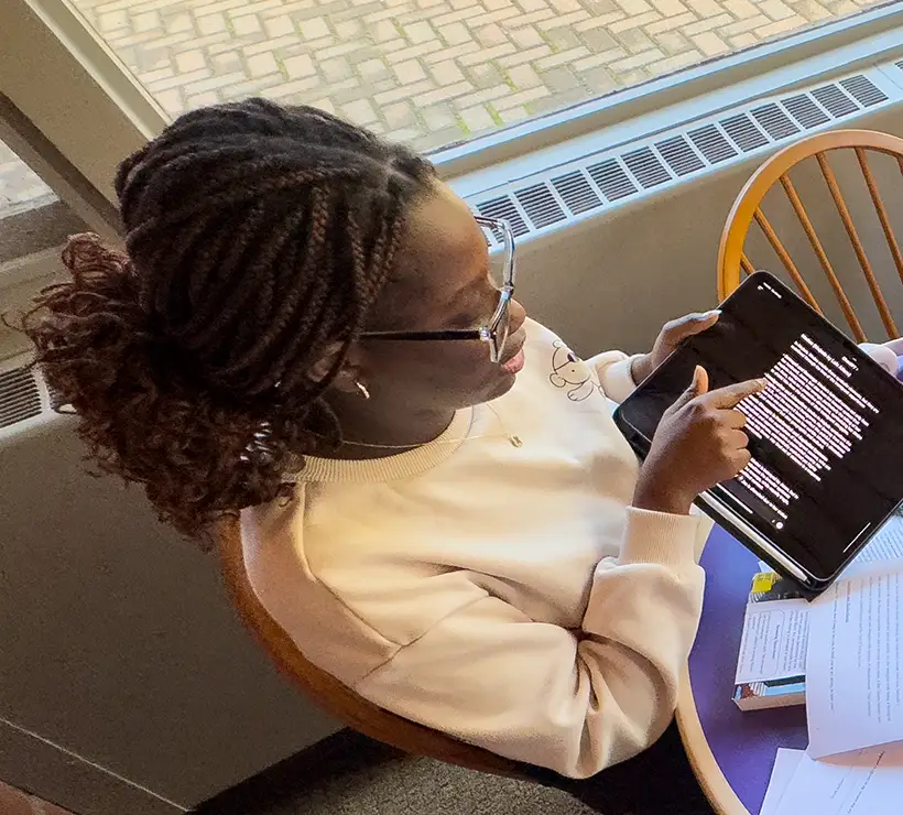 Oreoluwa Precious Ilori sitting at a table next to a window, pointing to something on the screen of her iPad.