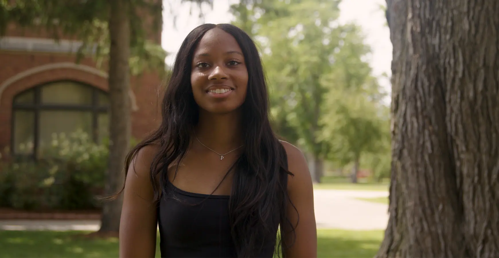 A student smiles at the camera outside of brick academic building.