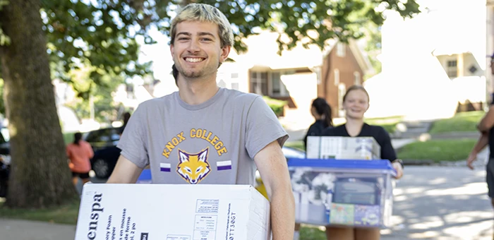 Students carrying boxes smiling at the camera.