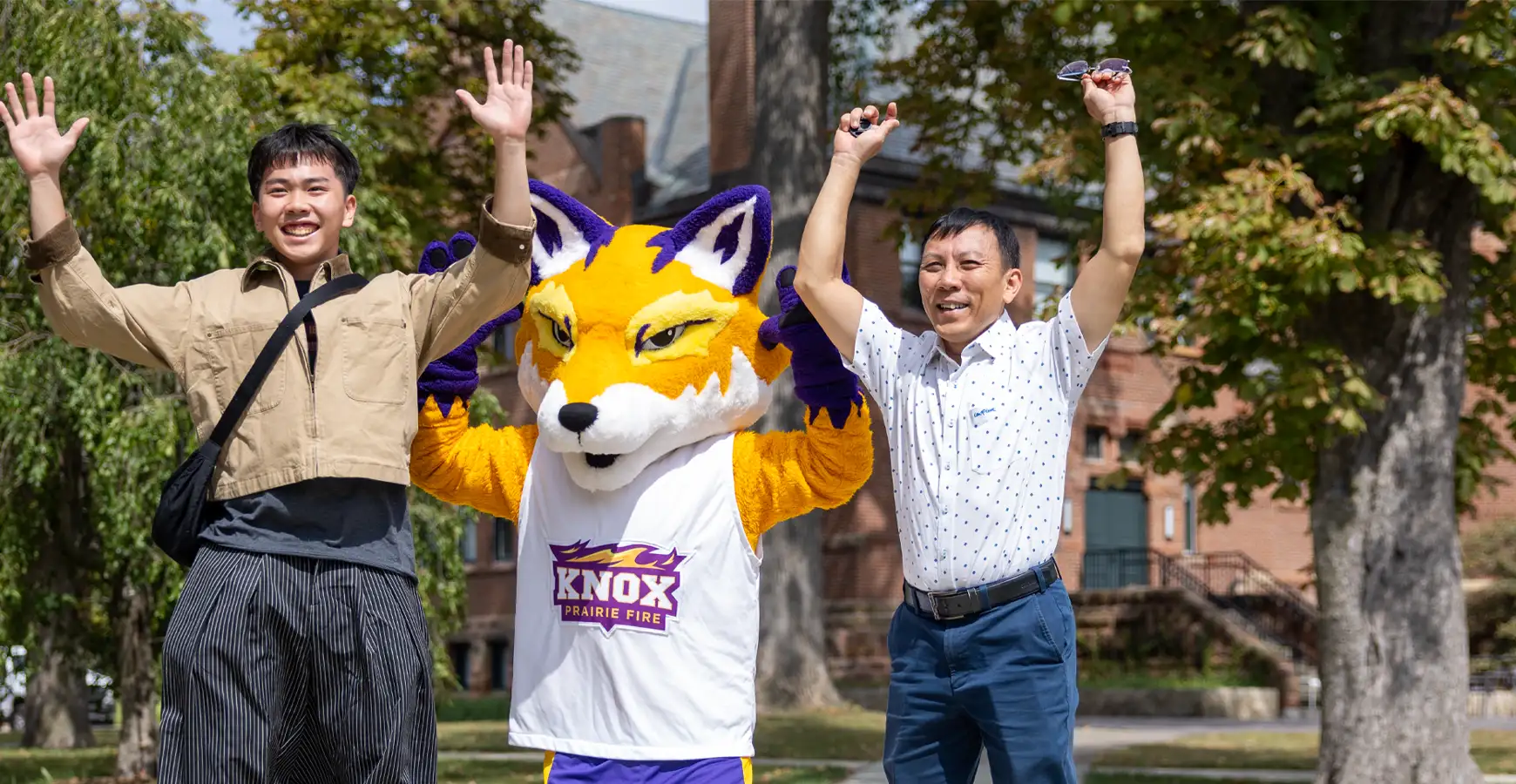A student and parent throw their hands up in the air. Blaze stands between them and does the same.