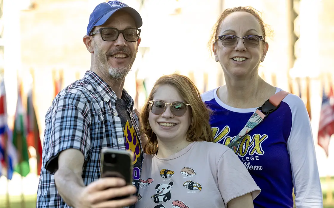 Three individuals take a selfie. One wears a shirt with writing Knox mom visible.