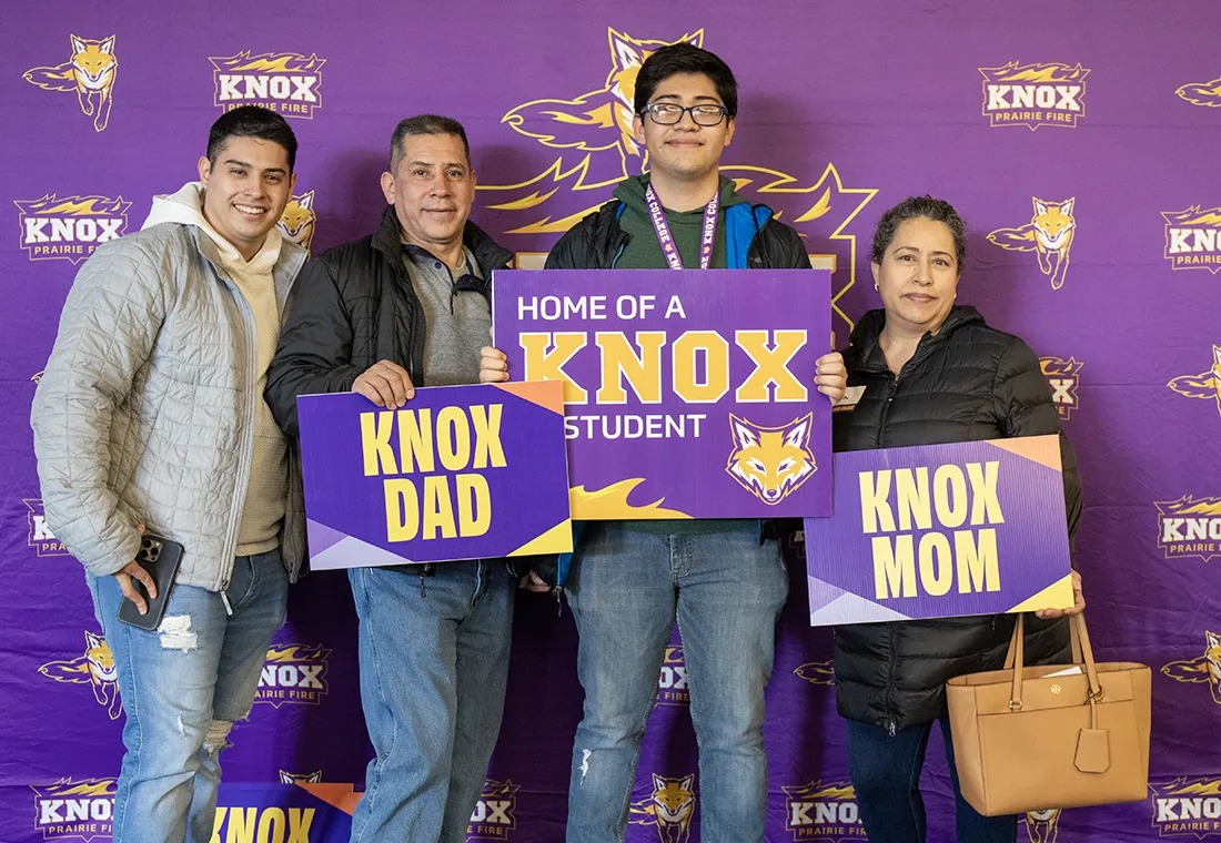 A family standing in front of a Knox step and repeat holding signs that say Knox Dad, Knox Bound, Knox Mom.