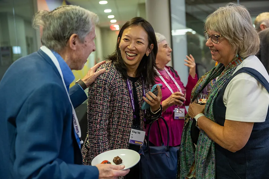 A group of alumni stand while talking and laughing with each other.