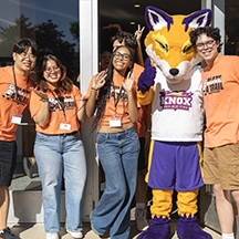 Four smiling Knox students pose with Blaze, the Prairie Fire Athletics mascot.