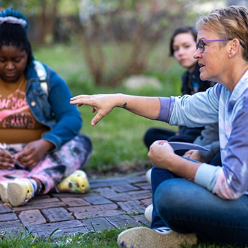 A Knox college professor and their students sitting on the campus lawn, deep in discussion.