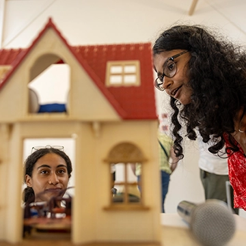 Two Knox students look at a dollhouse, one student is looking from above, while the other is peering in through a window.