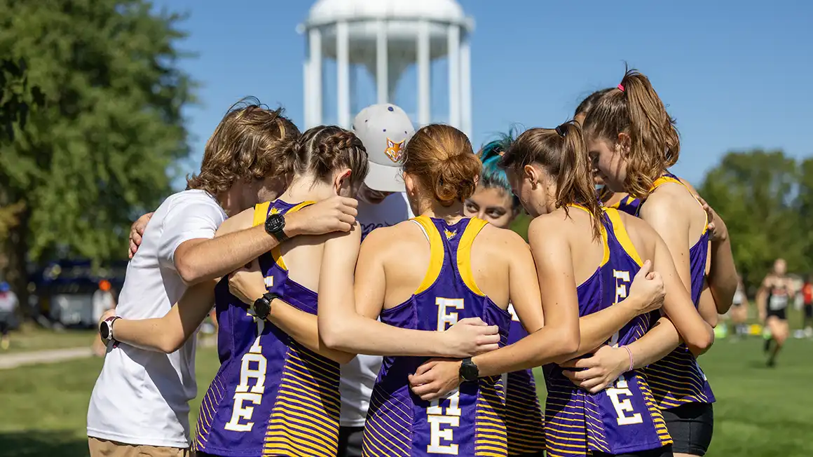 The Knox College women's cross country team huddles in front of a watertower.