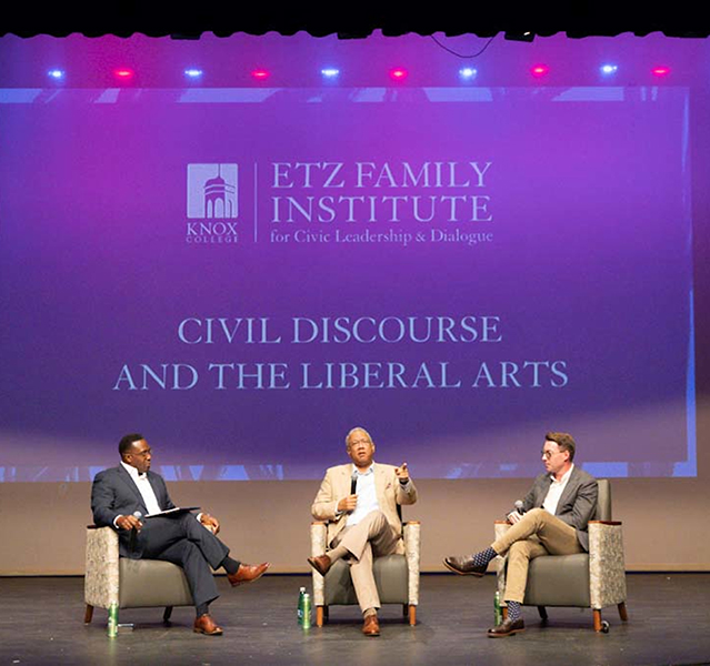 Three sitting on a stage people on a stage having a discussion in front of a backdrop that says Etz Family Institute for Civic Leadership & Dialogue.