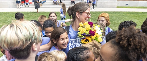 A group of Knox College four Kids students hug a teacher, who is holding a bouquet of lowers. 